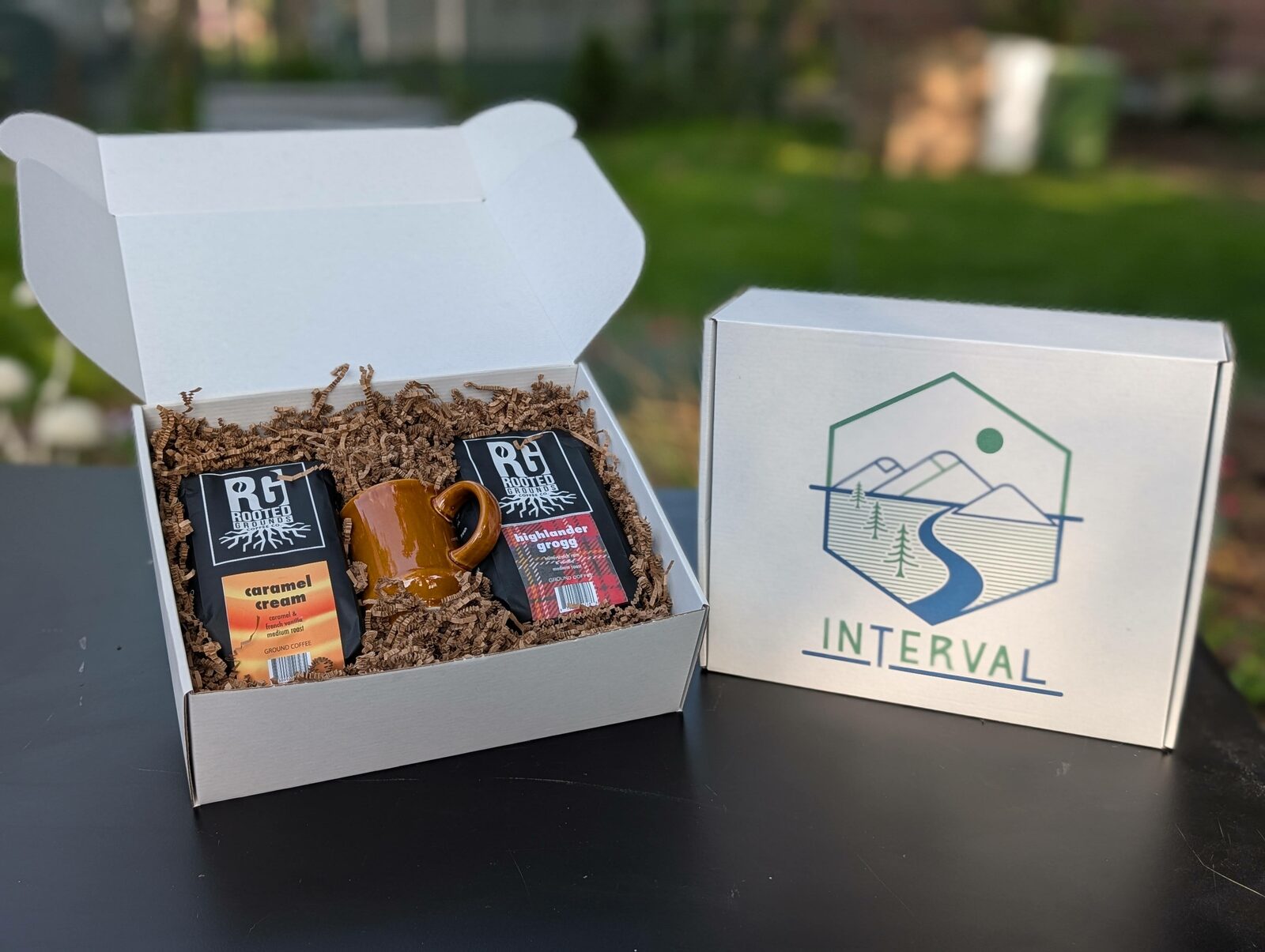 Open cardboard Interval kit with Rooted Grounds coffee bags and an amber ceramic mug